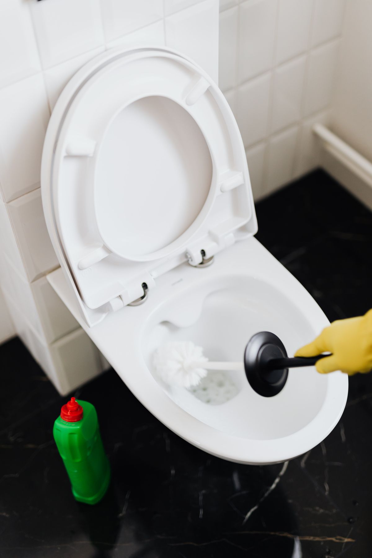 Gloved hand holding a plunger over a toilet bowl — the first safe check for a single slow fixture