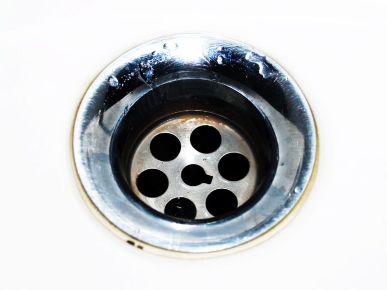 Close-up of a chrome sink drain in a white basin with water droplets