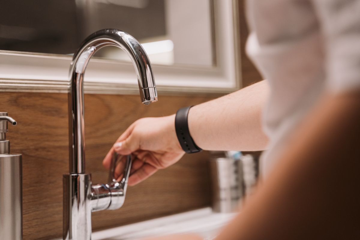 Hand on the lever of a modern chrome tap in a home bathroom, the kind of small repair covered by a standard call-out