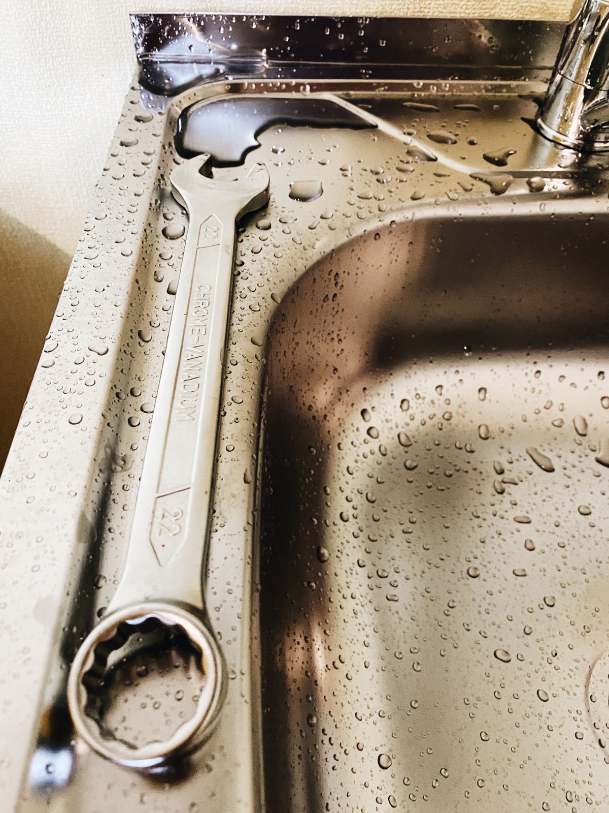 A spanner resting on a wet stainless steel kitchen sink while a burst pipe leak is contained